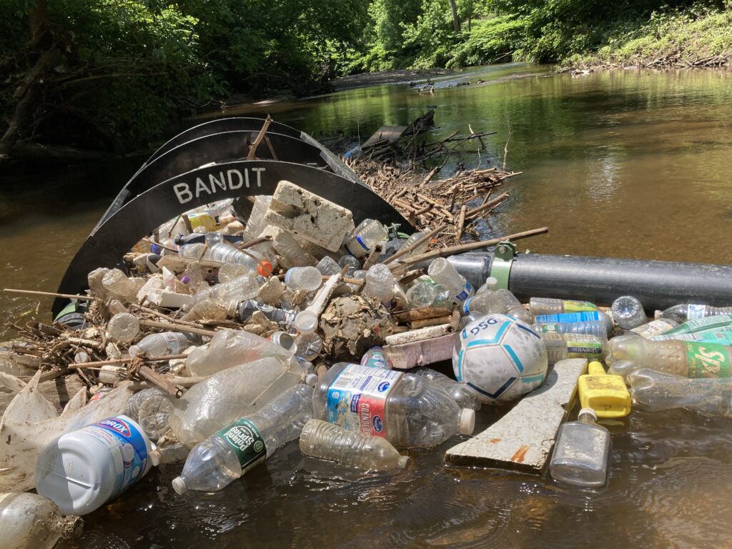 black plastic booms catching plastic, wood, and foam litter in a stream